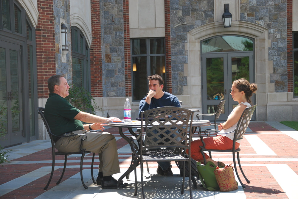 Mike Caslin speaks while two young adult students listen sitting at picnic table in outdoor courtyard
